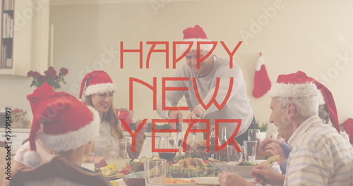 Image of happy new year text in red over family in santa hats at dinner table