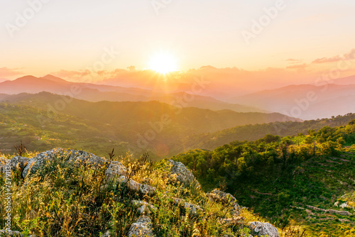 highland mountain landscape of beautiful sunset or sunrise with nice mountain peaks and slopes, green and golden hills and majestic cloudy sky on background