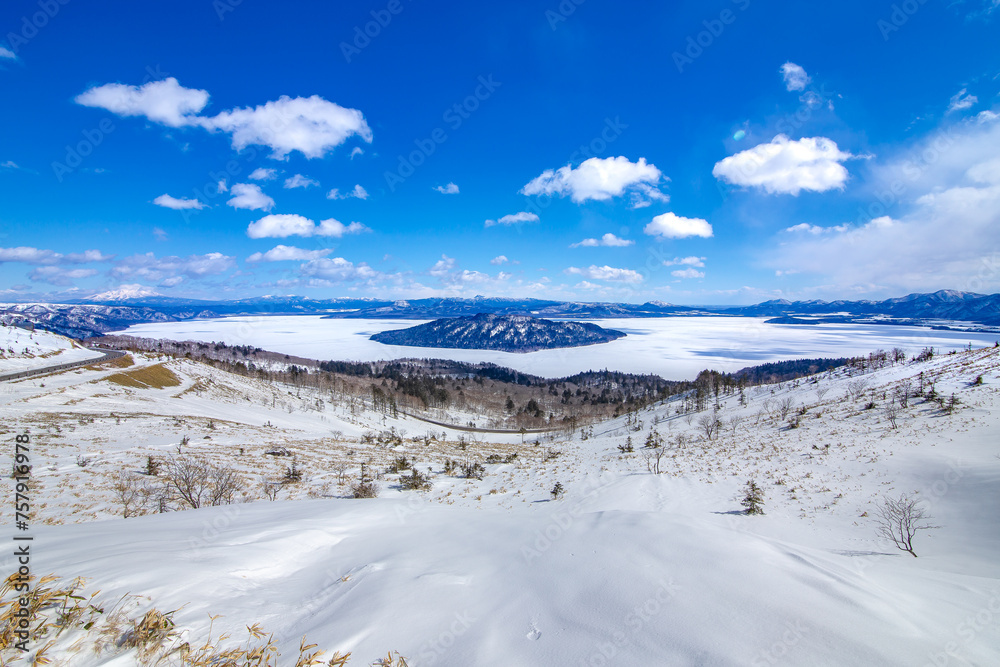 爽快な青空と雪に覆われた斜面と眼下の氷に覆われた湖。爽やかな印象の冬景色。北海道の美幌峠から見下ろす屈斜路湖。