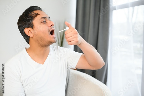 Indian man sick at home, cold, flu. A man uses a throat spray