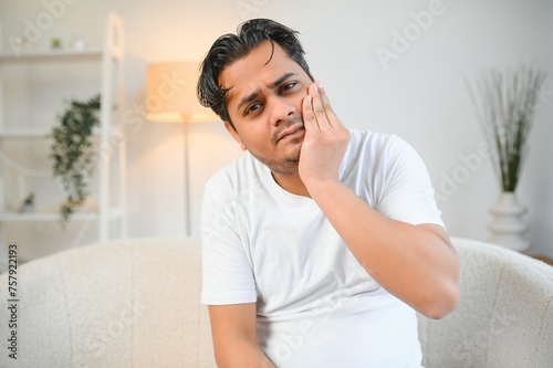 Toothache concept. Sad unhealthy indian or arabian guy touching cheek with hand with painful expression