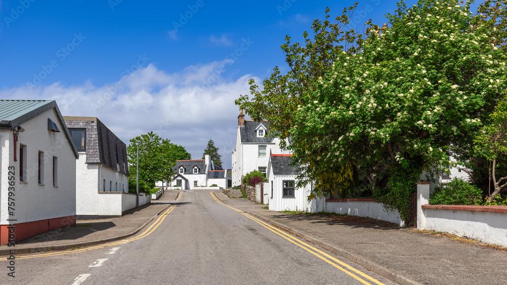 Obraz premium The quaintness of Ullapool is on display with white-rendered houses nestled among vibrant green foliage and flowering trees, beneath a blue sky. Highland Council, Scotland