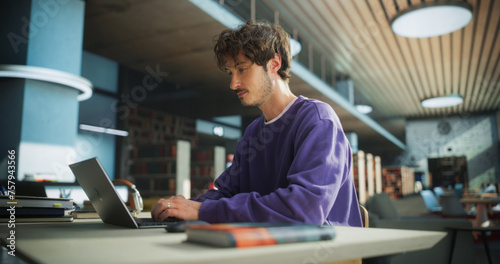 Student Studying in a Modern Library. Young Man Thinking and Problem Solving School Exercises. Male Using Laptop Computer to Work on a University Research Project Online
