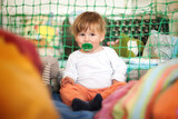 Toddler with tousled hair and curious eyes enjoy in bed with vivid green pacifier in their mouth