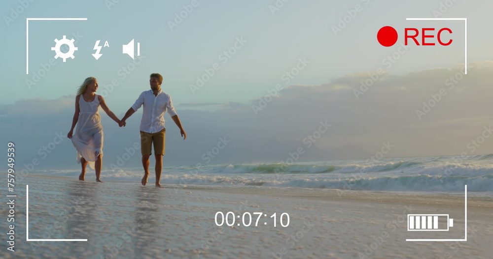 Fototapeta premium Couple holds hands on beach, viewed on a camera in 4K record mode.