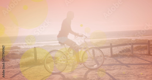 Yellow spots of light against caucasian woman riding a bicycle at the beach