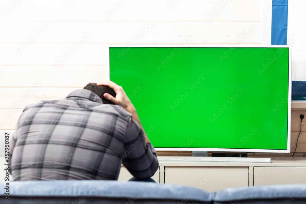 Shocked man on the couch watching tv. Bad news and Green screen concept