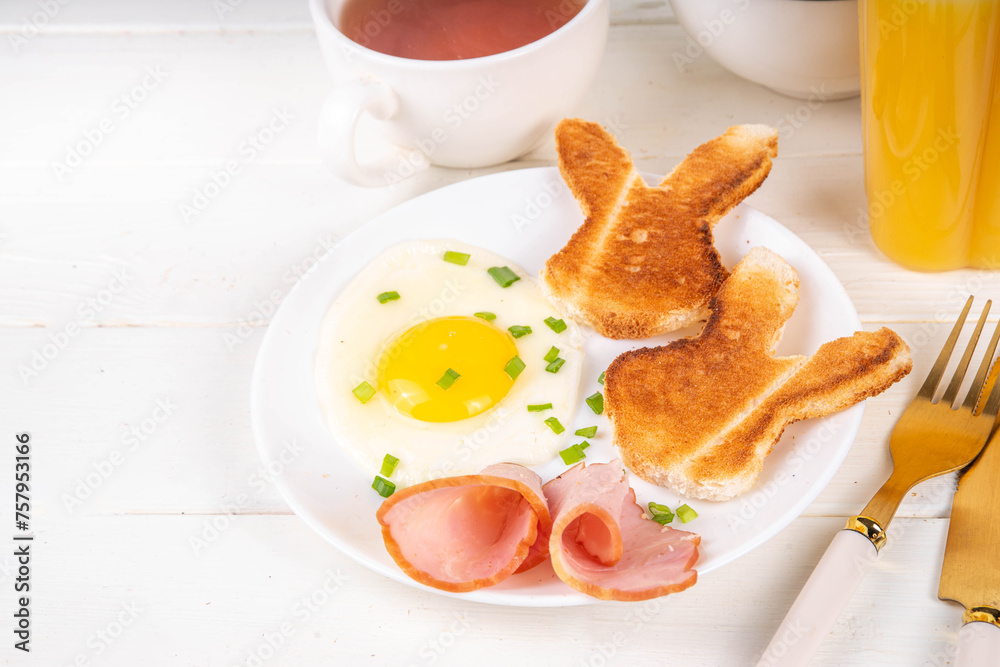 Easter breakfast or brunch with fried eggs, bacon slices and toasted bread shaped in form of bunny rabbits face, with spring flowers and Easter chocolate eggs on white wooden table copy space Easter breakfast or brunch with fried eggs, bacon slices and toasted bread shaped in form of bunny rabbits face, with spring flowers and Easter chocolate eggs on white wooden table copy space