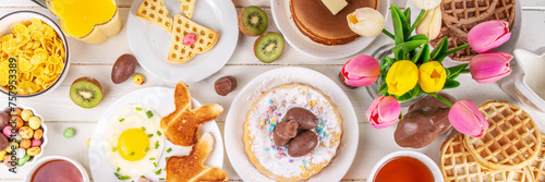 Easter holiday sweet breakfast, brunch. Easter decorated belgian waffles, pancakes, breakfast cereals and milk, fried eggs with toasts and bacon, Easter chocolate eggs and bunny, with spring flowers