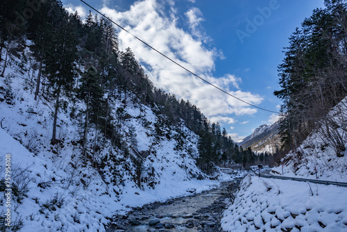 visuale panoramica su di un ambiente  naturale di montagna, all'ombra, completamente freddo e coperto di neve, nel nord Italia, sotto un cielo parzialmente sereno, di pomeriggio, in inverno photo