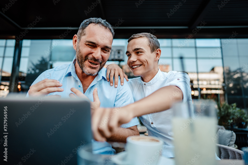 Handsome and happy father and his teenager son sitting in a restaurant and talking. Handsome and happy father and his teenager son sitting in a restaurant and talking.