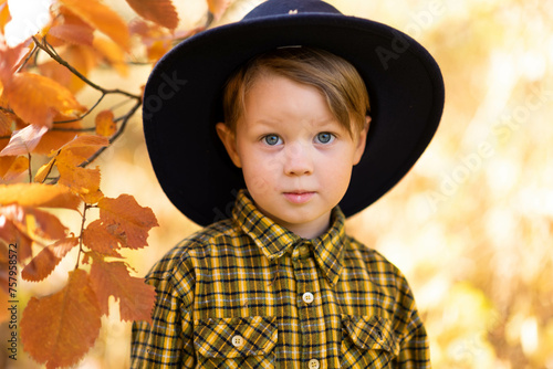 Autumn portrait of a little cute fair-haired and smiling boy in a wide-brimmed hat in the park