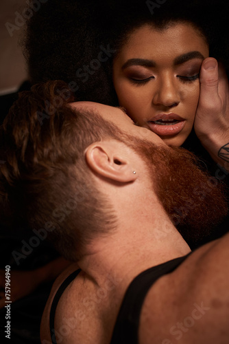 bearded man with tattoos touching face of curly african american woman while seducing her on bed © LIGHTFIELD STUDIOS
