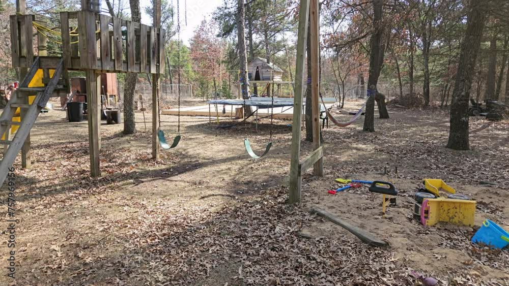 Playground with swings and sandbox and trampoline in back yard with tree house and ice rink in background in sunny dry winter season Playground with swings and sandbox and trampoline in back yard with tree house and ice rink in background in sunny dry winter season