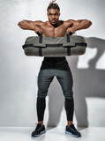 Sporty man working out, holds heavy sandbag. Photo of man with naked torso on grey background. Strength and motivation
