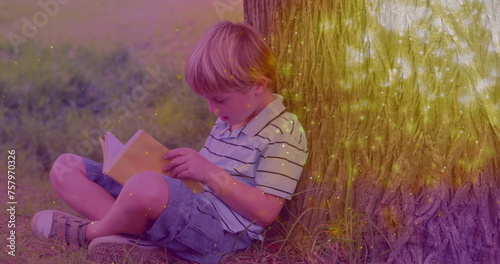 Image of glowing spots over caucasian boy reading book