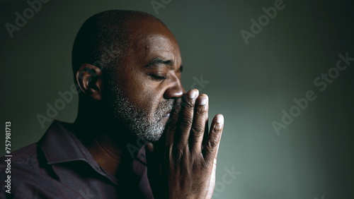 Картината върху платно One religious black senior man in contemplative PRAYER at home in dimly lit room with eyes closed having HOPE and FAITH during challenging times