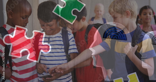 Image of puzzle pieces over diverse schoolchildren using smartphone