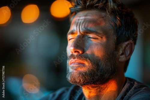 The photo shows a mature man with a hidden face, gazing away with a serious expression amidst a warm lit background