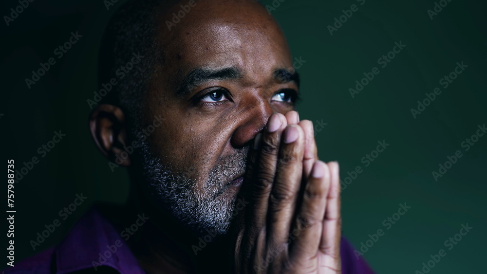 Spiritual African American senior person praying to GOD, closing eyes in contemplation with hands clenched together. Faithful man asking for HELP and SUPPORT - obrazy, fototapety, plakaty 