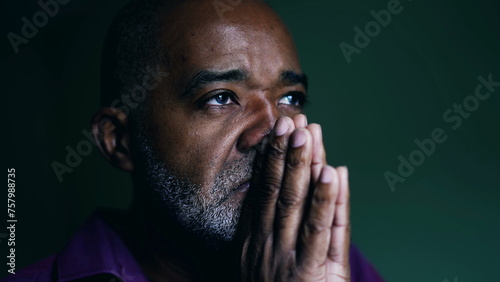 Spiritual African American senior person praying to GOD, closing eyes in contemplation with hands clenched together. Faithful man asking for HELP and SUPPORT photo