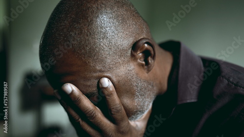 One middle-aged black 50s man in despair covers face with hands struggling with crisis. South American person in dimly lit room feeling desperation and loneliness during challening times