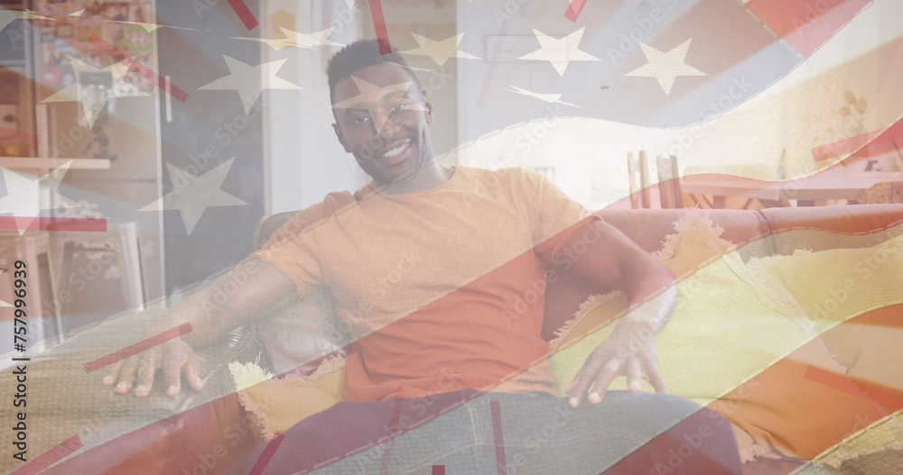 Image of flag of united states of america over happy african american male sitting on couch
