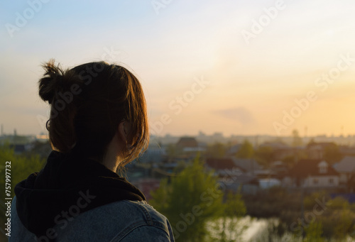 Photo of a girl from behind who looks at the evening landscape at sunset