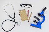 Top view of microscope, stethoscope, eyeglasses and notebook with pen