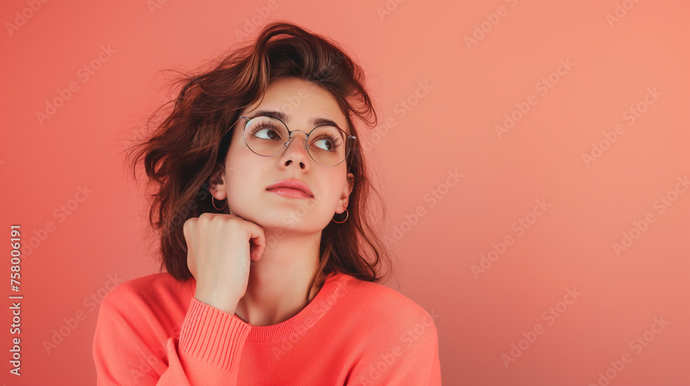 Portrait of young woman with dreamy cheerful expression, looking right, thinking, wearing round glasses on Coral color background professional photography Portrait of young woman with dreamy cheerful expression, looking right, thinking, wearing round glasses on Coral color background professional photography