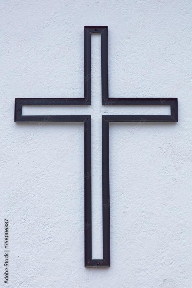 Closeup of black metal cross on a white stone building exterior wall.