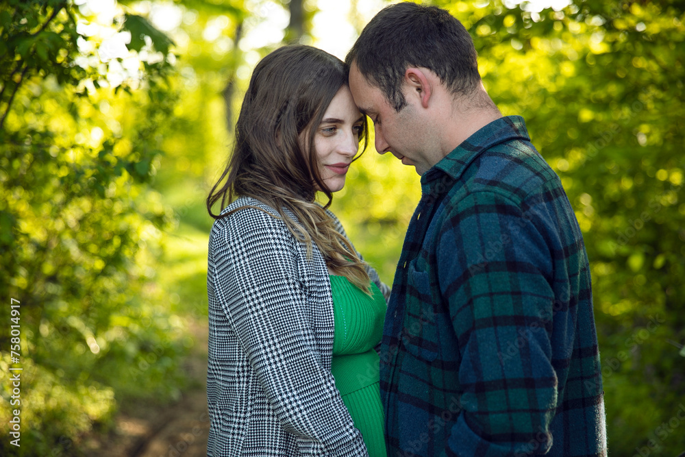 Horizontal view of a attractive couple expecting a baby spend time outdoors on a summer day, being hugged. Horizontal view of a attractive couple expecting a baby spend time outdoors on a summer day, being hugged.