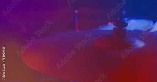 Image of hands of drummer playing drum kit, cymbal in foreground, red and blue light
