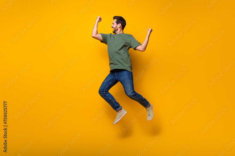 Full size photo of handsome young guy raise fists winning jumping wear trendy khaki outfit isolated on yellow color background