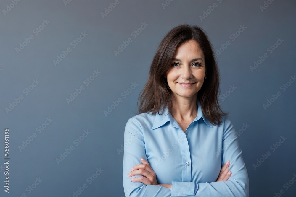 Middle-aged woman wearing a blue office shirt confidently standing with arms crossed on a dark blue background with copy space. Middle-aged woman wearing a blue office shirt confidently standing with arms crossed on a dark blue background with copy space.