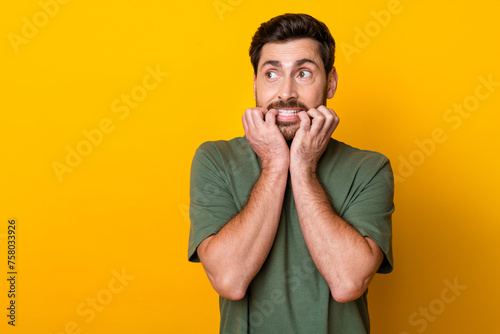 Photo of guilty scared man wear khaki t-shirt biting fingers looking empty space isolated yellow color background