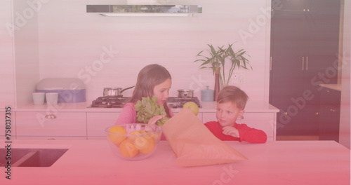 Caucasian brother and sister removing vegetables from paper bag in the kitchen