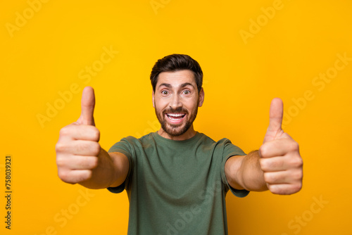 Photo of cheerful excited man wear khaki t-shirt showing you two thumbs up isolated yellow color background © deagreez