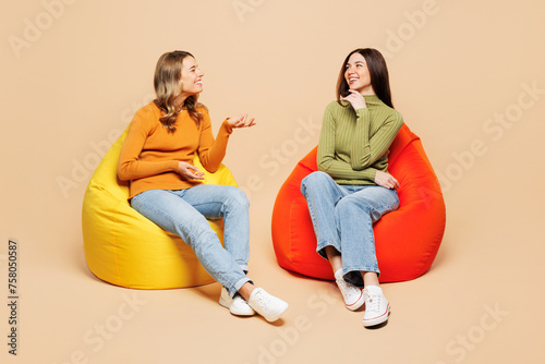 Full body young friends two women they wear orange green shirt casual clothes together sit in bag chair talk with each other isolated on plain pastel light beige background studio. Lifestyle concept.