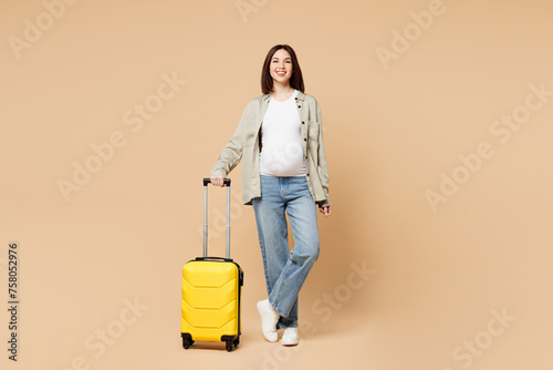 Traveler pregnant woman wears grey casual clothes hold suitcase bag ticket walk go isolated on plain beige background. Tourist travel abroad in free time rest getaway. Air flight trip journey concept.