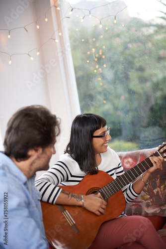 Couple, woman and play guitar in living room for men, chilling and enjoying together on couch. Married, wife and husband with smile on sofa to bond, entertainment and listen to musical instrument
