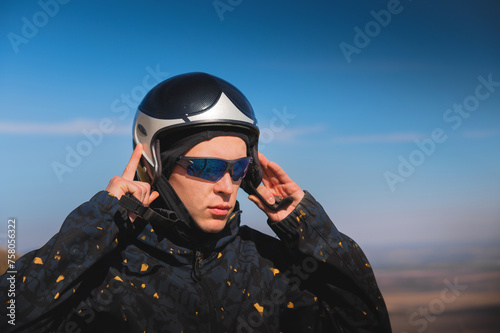 A young male paraglider in sunglasses fastens his helmet on a sunny day. Preparing for paragliding © yanik88