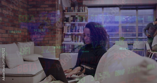 Image of financial data over biracial businesswoman working on laptop in office