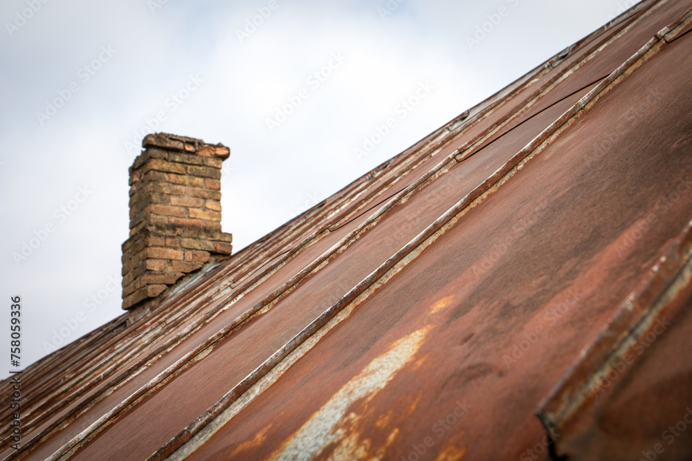 Old rusty metal roof with patches. Repair and renovation. Brick chimney