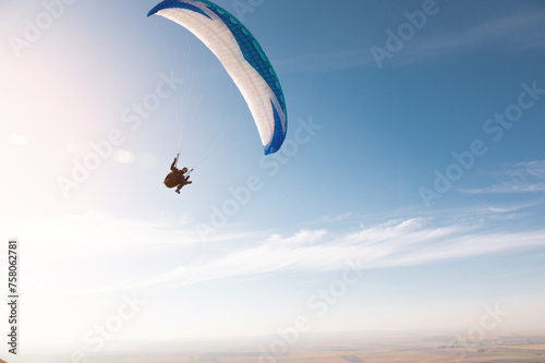 A paraglider with a blue parachute fly. A male flyght on the sky and lifts a paraglider into the air photo