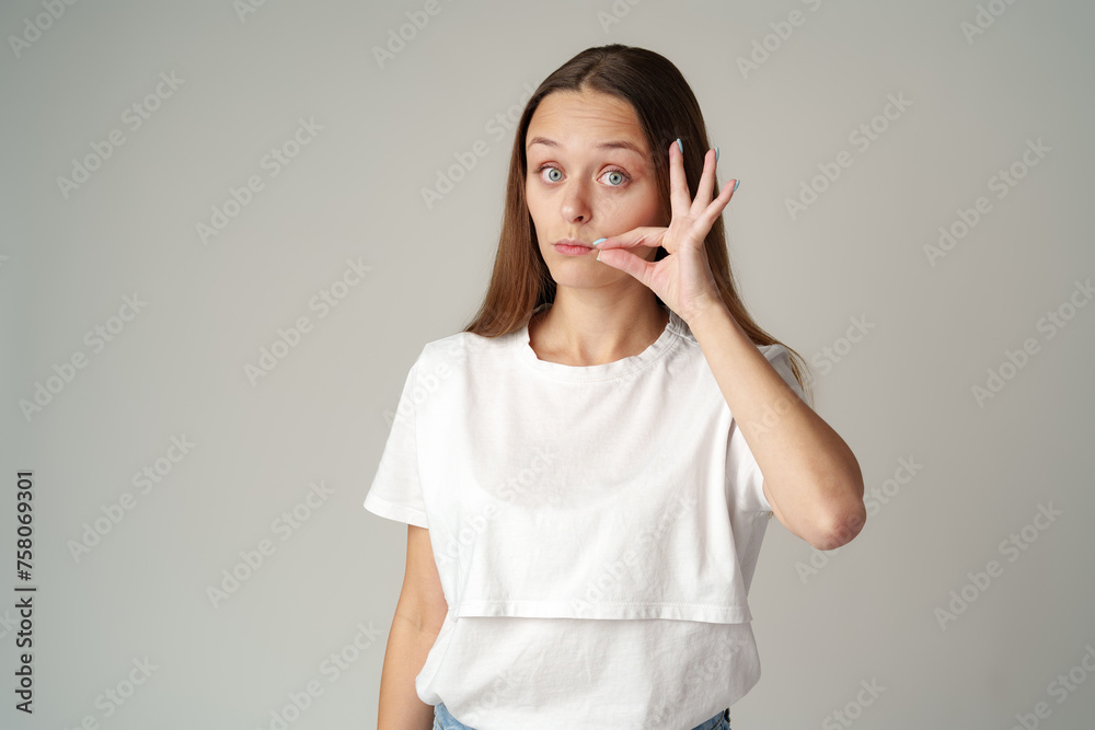 Young pretty woman saying hush be quiet hand sign on gray background Young pretty woman saying hush be quiet hand sign on gray background