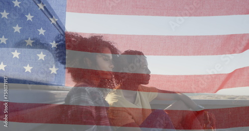 Image of American flag waving over biracial couple on beach by seaside on summer holiday road trip i