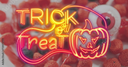Neon trick or treat text banner with pumpkin icon against scary eye toy and halloween candies