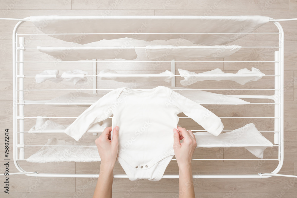 Φωτογραφία Young adult mother hands holding and hanging white clean baby bodysuit on drying rack at home room