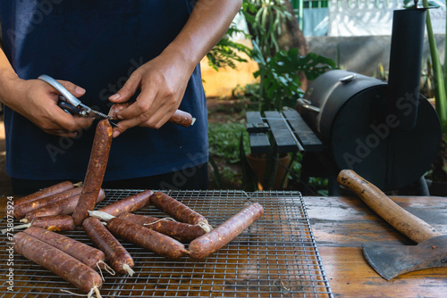 A man is cutting a sausage link that uses collagen casing, it will be cooked using the smoking technique photo